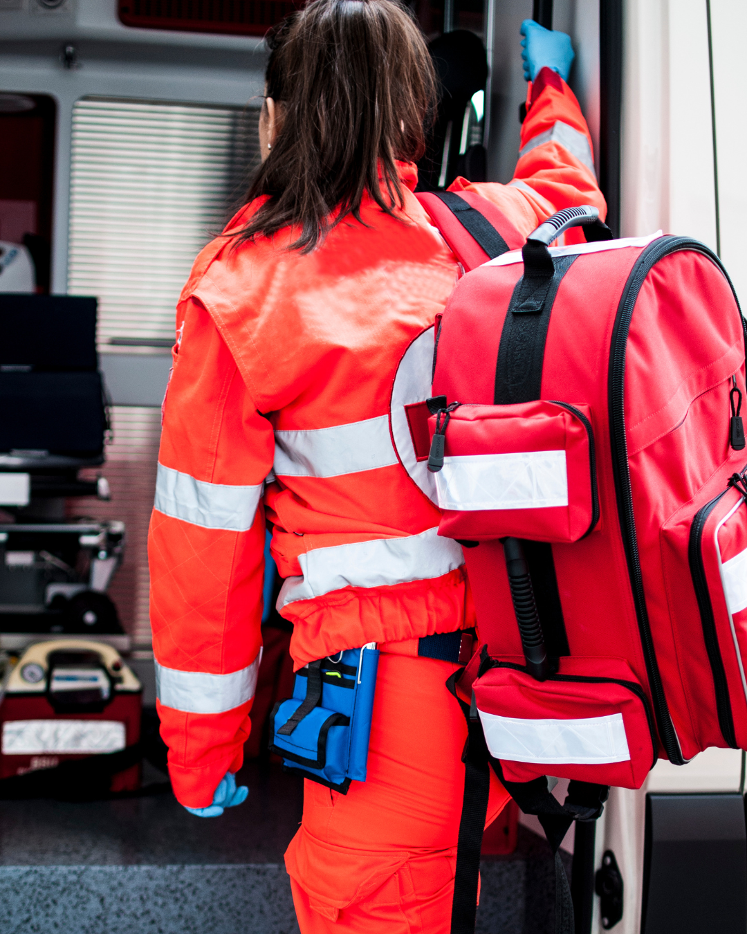 Paramédica con uniforme de emergencia roja ingresando a ambulancia equipada, atención médica urgente y primeros auxilios